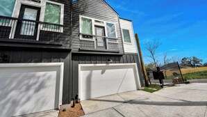 A two-story house with a garage, a balcony, and a fenced yard. - Modern 2BR Townhome Near NRG • Med Center • Downtown w/ Garage (Houston)