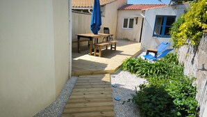 A wooden deck leading to a patio area with a table and chairs, surrounded by plants and a small wall. - Fisherman's cottage in the heart of La Chaume, 5 minutes from the quays and the wild coastline (Les Sables-d'Olonne)