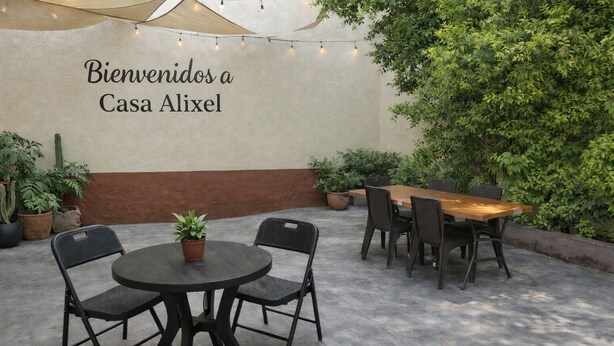 An outdoor patio with a round table and chairs, a wooden dining table with chairs, and a wall with a welcome sign.