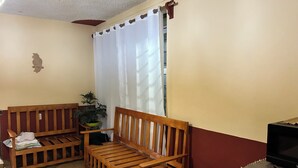 A room with a wooden sofa, a small table, a potted plant, a television, and a window with curtains.