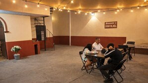 A group of people seated at a table in a room with a staircase and a sign reading 'Bienvenidos a CASA ALXEL'.
