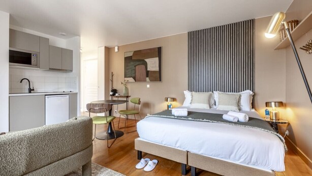 Ein modernes Hotelzimmer mit Bett, Nachttischen, Schreibtisch und einer Küchenzeile.