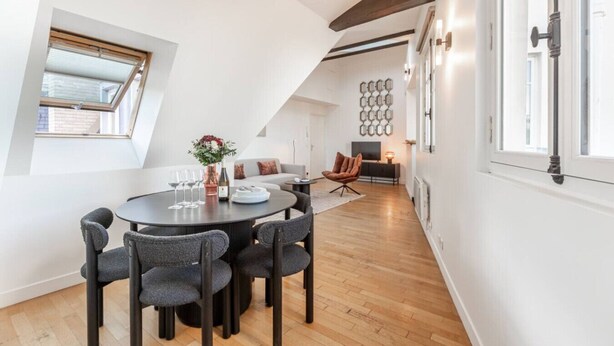Un loft moderno con comedor, que incluye una mesa redonda y sillas, un sofá y un televisor al fondo.