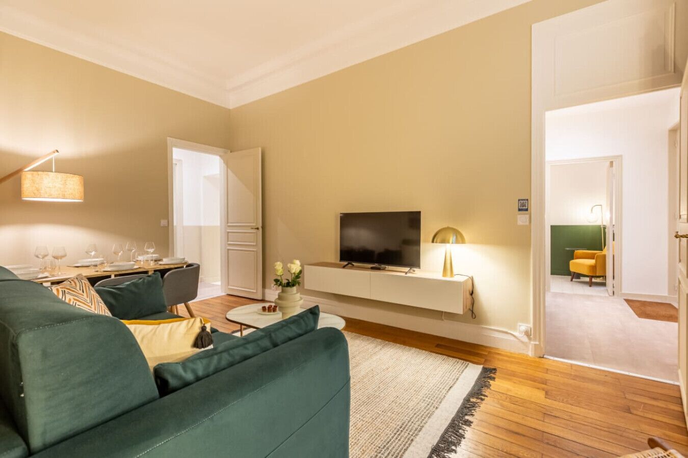 A modern living room with a green sofa, a flat-screen TV, and a dining area with a table set for four.