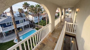 Uma varanda com vista para uma piscina, palmeiras e casas vizinhas.