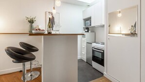 Una cucina compatta con isola centrale, un forno a microonde e un piano cottura. Ci sono due sgabelli da bar e un tavolino con un vaso e una bottiglia.