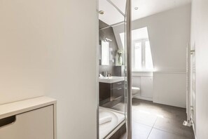 A modern bathroom with a glass shower enclosure, a white sink, and a toilet. - Hoche - Arc de Triomphe - 2p - Bail Mobilité (Paris)