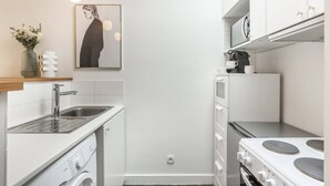 Una cucina compatta con lavatrice, lavello, fornello e microonde.