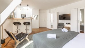 Una camera d'albergo moderna con un letto, una scrivania, due sgabelli da bar, una sedia, una TV e un armadio.