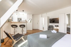 A modern hotel room with a bed, a desk, two bar stools, a chair, a TV, and a wardrobe. - Hoche - Arc de Triomphe - 2p - Bail Mobilité (Paris)