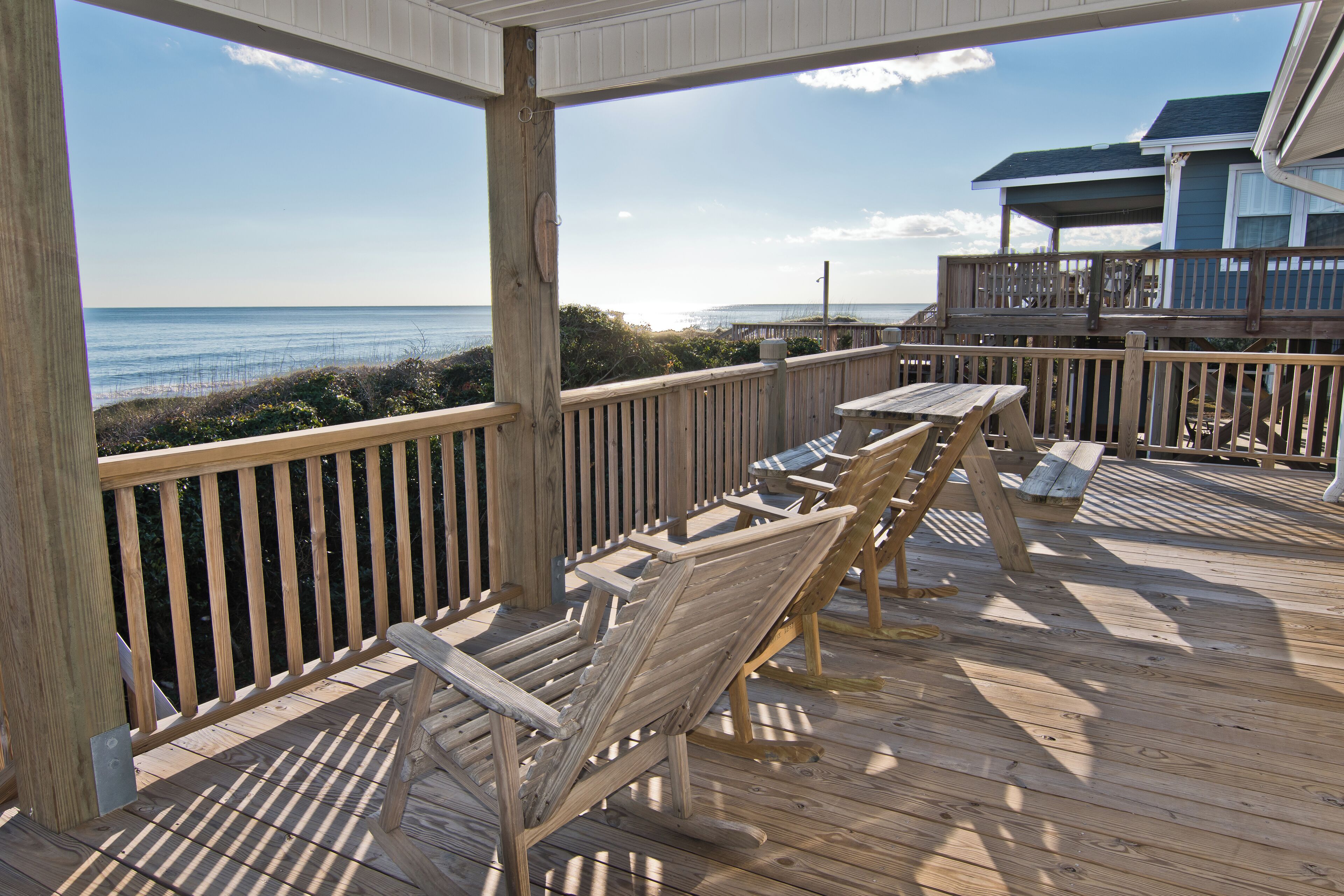 A wooden deck with outdoor furniture, a railing, and a view of the ocean.