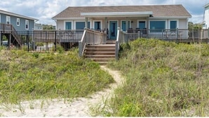 Una casa frente a la playa con un muelle de madera y escaleras que conducen a la entrada.