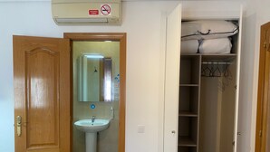 A room with a wooden door, a white sink, a mirror, and a closet with hanging clothes. - Hostal Retiro (Madrid)
