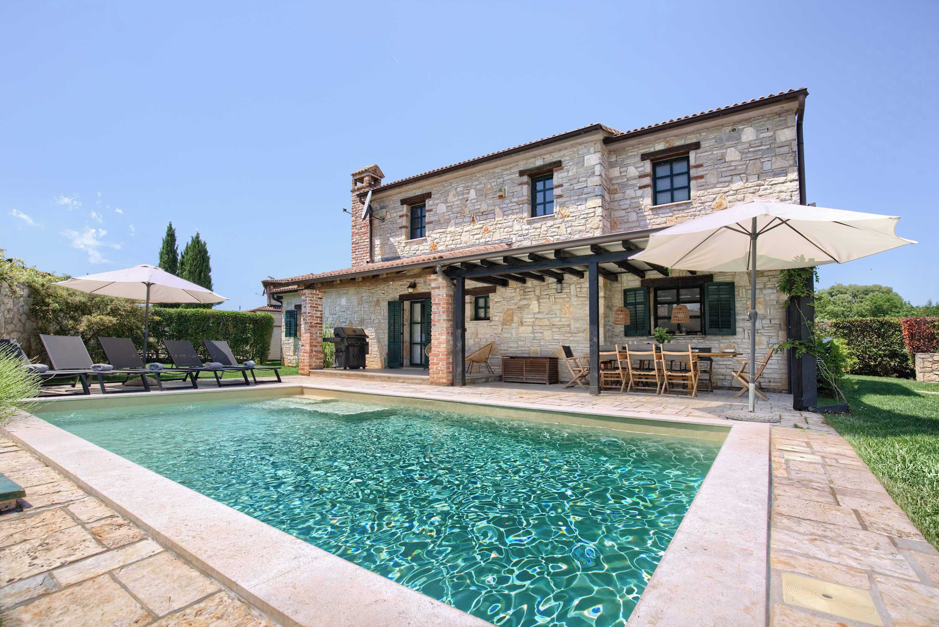 A stone building with a pool, outdoor seating, and a pergola.