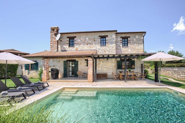 Una casa de piedra con piscina, muebles de exterior y zona de barbacoa.