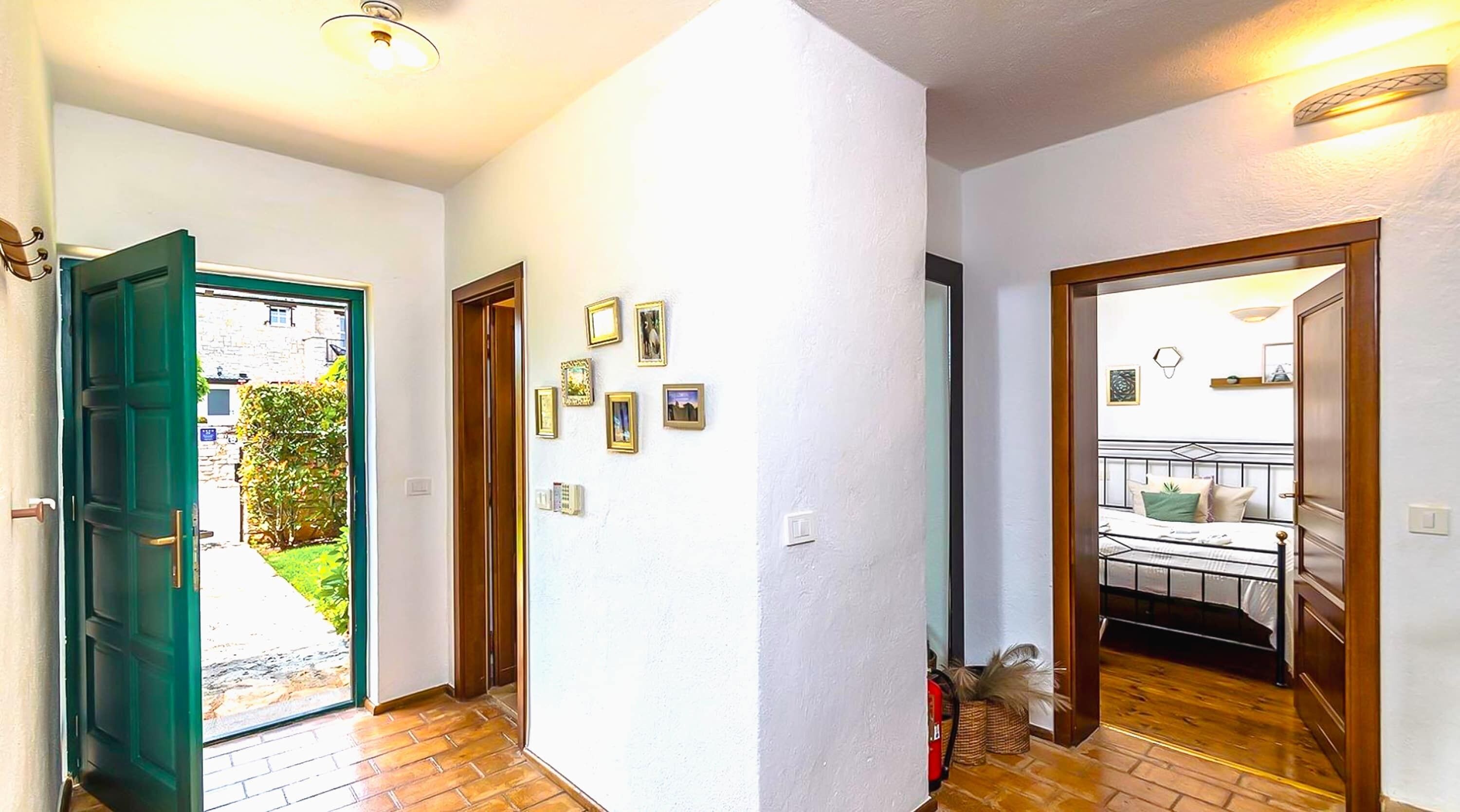 A hallway with a green door leading outside, a wooden door to a bedroom, and a wall with framed pictures.