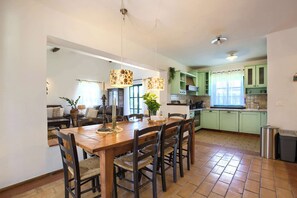 Un comedor con mesa y sillas de madera, una cocina con armarios verdes y una ventana con cortinas.
