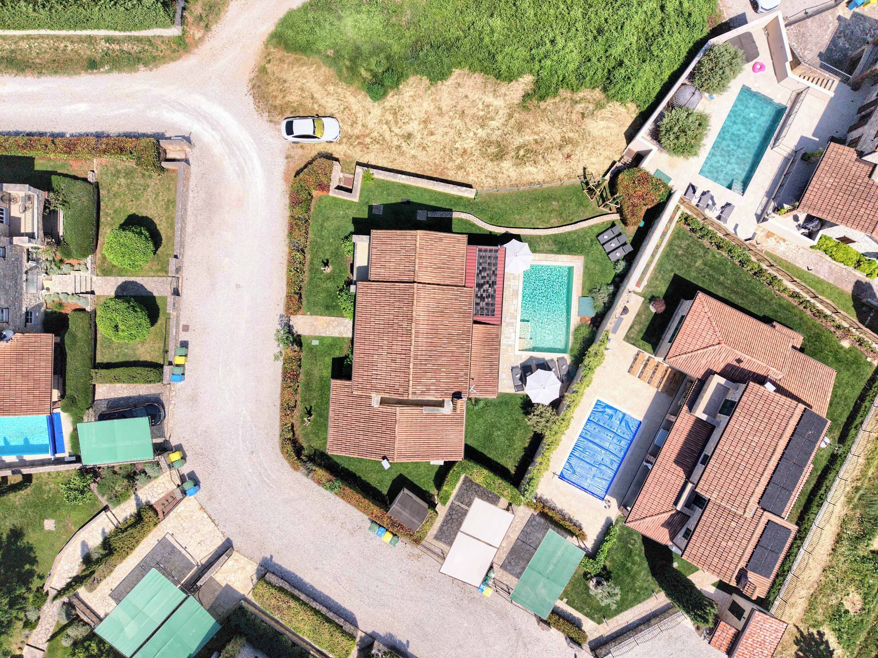 Luchtbeeld van een woongebied met meerdere huizen, een zwembad en een weg.