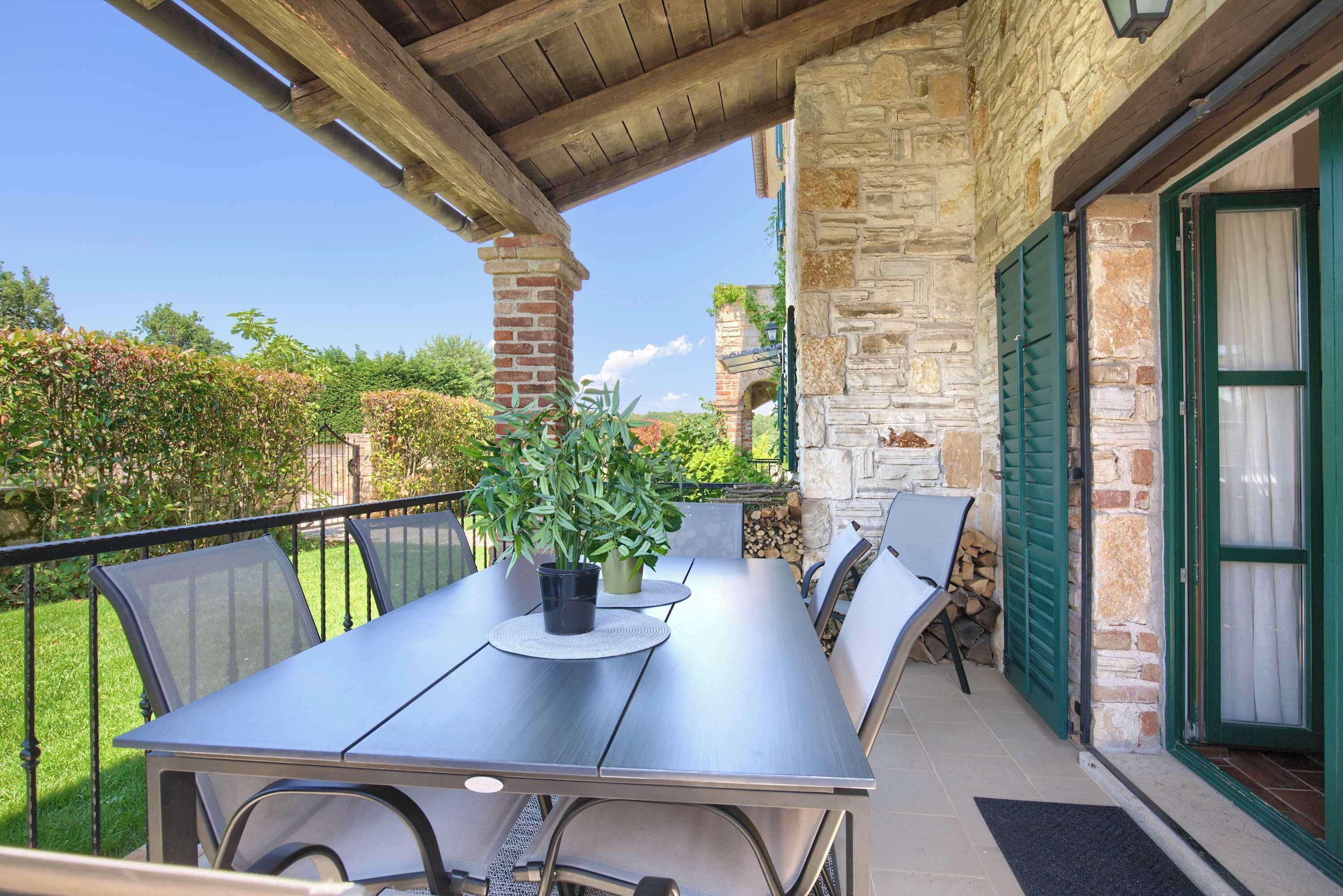 Eine Terrasse im Freien mit Tisch und Stühlen, Steinmauern und Blick auf den Garten.