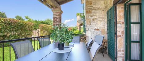 Eine Terrasse im Freien mit Tisch und Stühlen, Steinmauern und Blick auf den Garten.