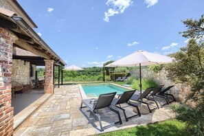 A poolside area with a stone patio, lounge chairs, and umbrellas.