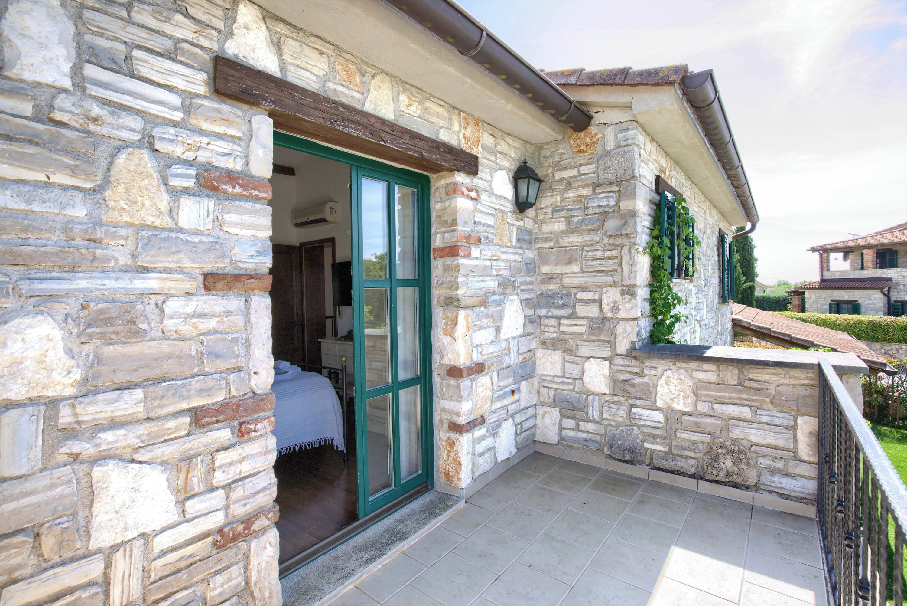 Un bâtiment en pierre avec une porte verte, un balcon et un mur de pierre recouvert de lierre.