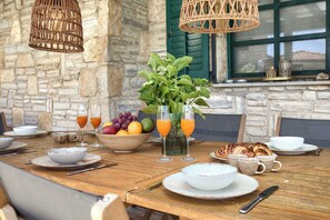 A wooden dining table set with plates, glasses, and a bowl of fruit.