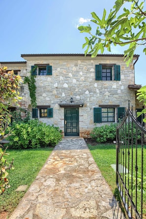 A stone building with a central entrance, green shutters, and a stone pathway leading to the door.