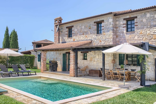 A stone building with a swimming pool, outdoor seating, and a barbecue area.