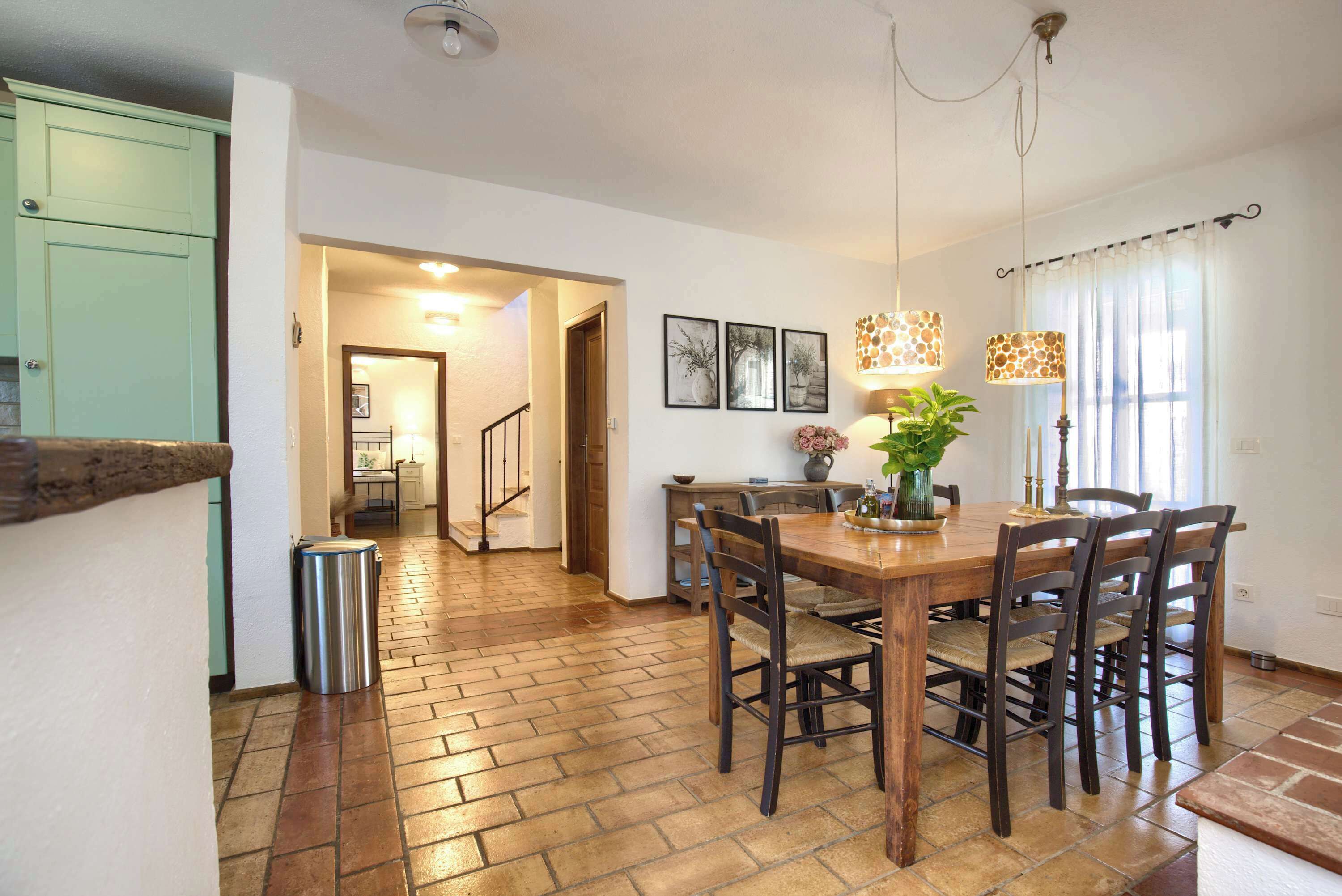 A dining area with a wooden table and chairs, a trash can, and a staircase leading to another room.