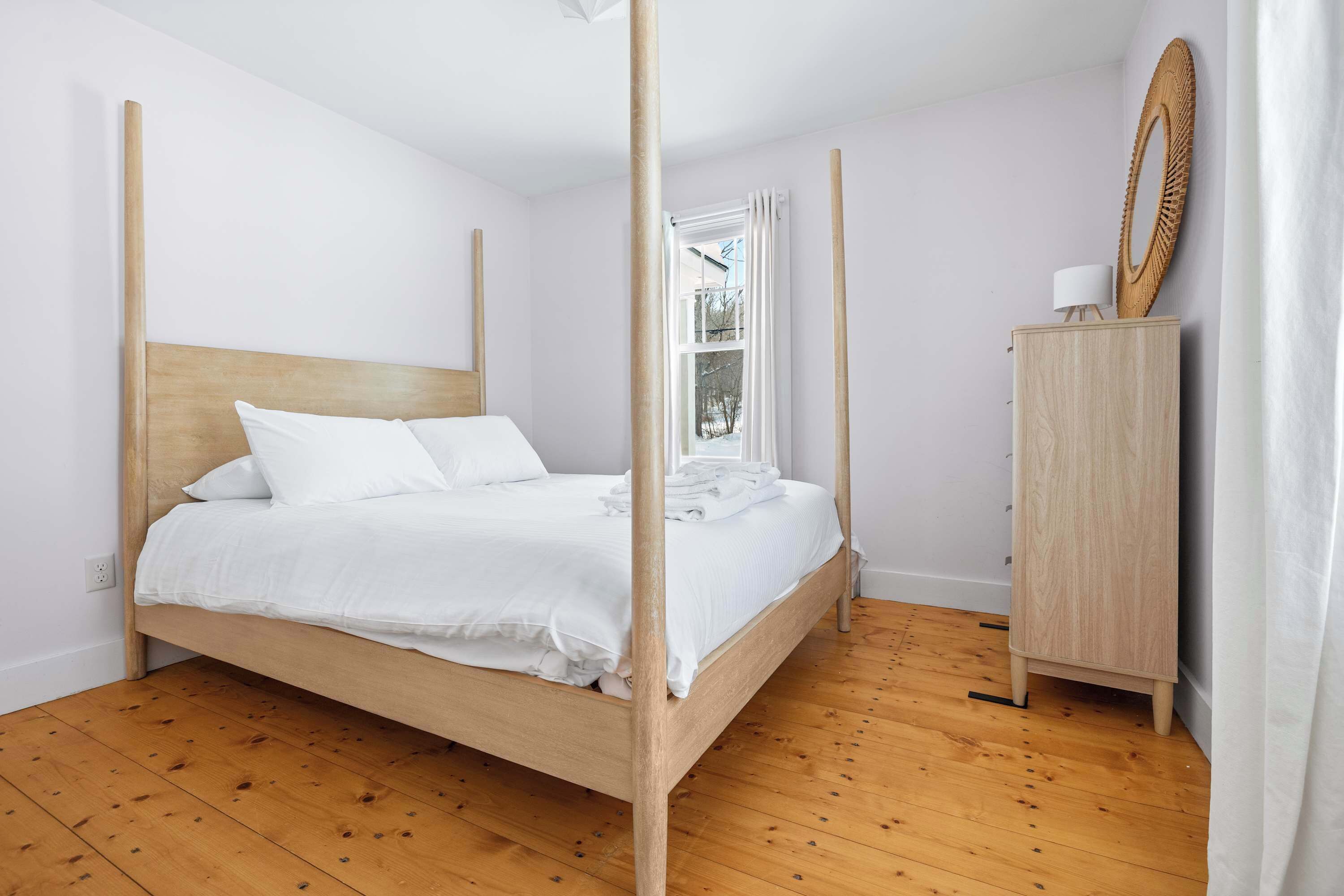 A four-poster bed with white bedding, a wooden headboard, and a wooden wardrobe with a mirror.