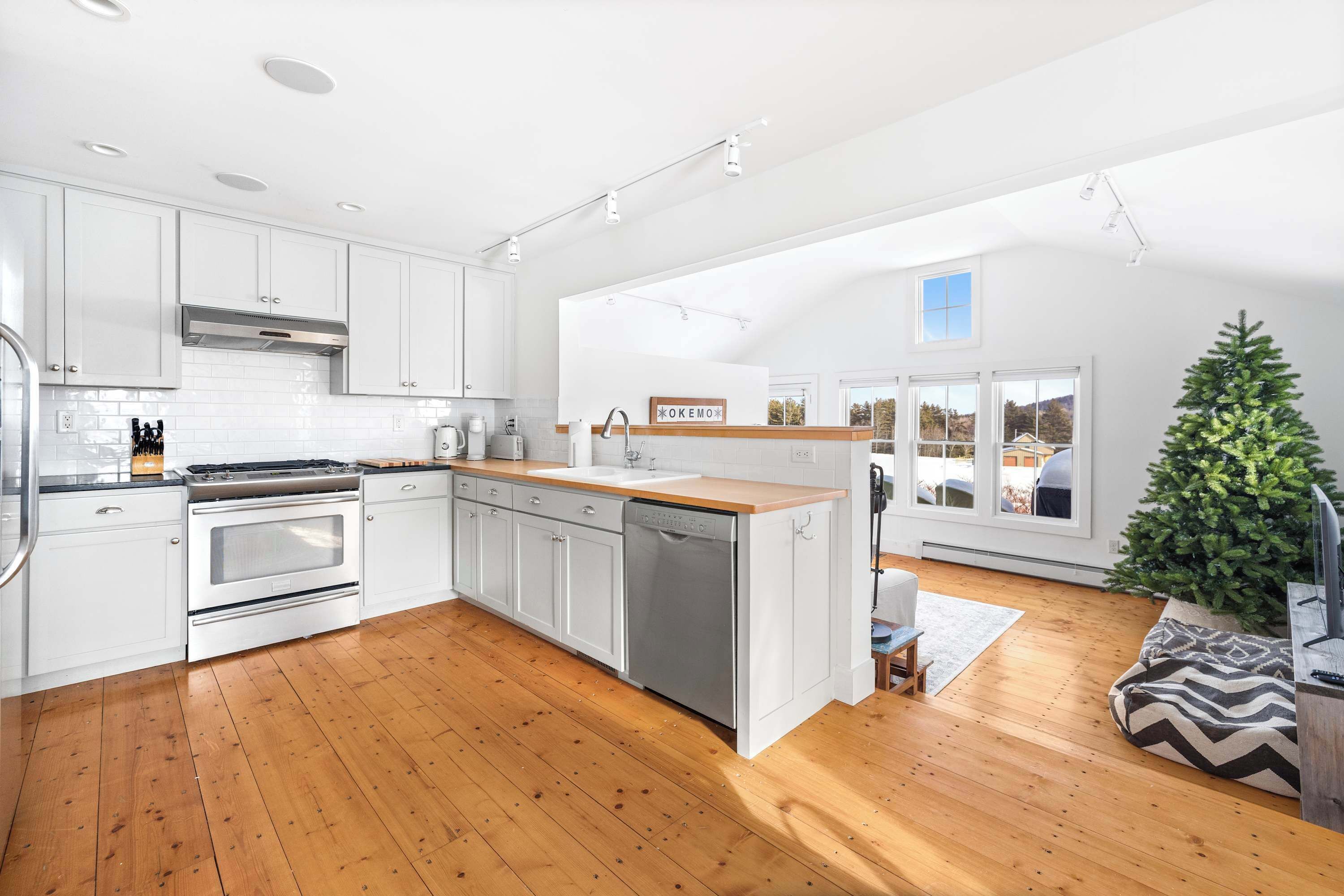 A modern kitchen with white cabinets, stainless steel appliances, and a wooden floor.