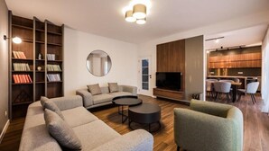 Un salon moderne avec un canapé d’angle, une table basse ronde, une bibliothèque et un téléviseur.
