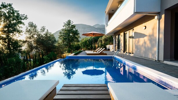 Une piscine dotée de chaises longues et d’un parasol, entourée d’arbres et offrant une vue sur la montagne.
