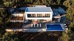 Une maison moderne à deux étages avec une piscine, entourée d’une végétation dense.