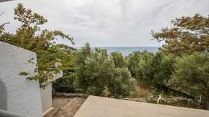 A balcony with a view of the sea, surrounded by greenery and a white wall. - Entire Cottage in Kerames, Crete – 250 m from the Beach (Agiou Vasileiou)