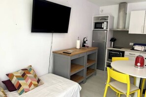 A compact room with a bed, a small desk with a chair, a television, a kitchenette, and a dining area with a table and chairs. - Cosy 2-4 pers - Private parking lot - Walking distance to beaches & Exflora Park (Antibes)