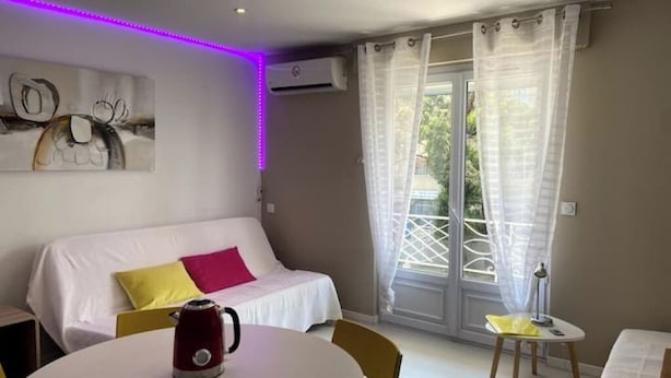 A room with a bed, a table with a kettle, a chair, and a window with curtains. - Cosy 2-4 pers - Private parking lot - Walking distance to beaches & Exflora Park (Antibes)