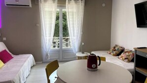 A hotel room with two beds, a round table with a kettle, a TV on the wall, and a balcony with a view. - Cosy 2-4 pers - Private parking lot - Walking distance to beaches & Exflora Park (Antibes)