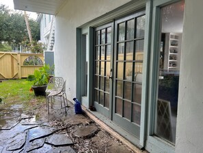 A covered patio area with a sliding glass door, a potted plant, a chair, and a blue water container. - Private, large 2-bedroom house with a balcony in beautiful Bayou St. John. (New Orleans)