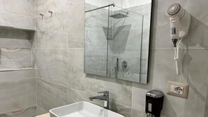Ein modernes Badezimmer mit einer Duschkabine aus Glas, einem weißen Waschbecken und einem an der Wand befestigten Föhn.