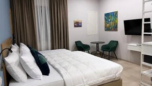 Ein Hotelzimmer mit einem Bett, zwei Stühlen, einem kleinen Tisch, einem Fernseher und Bildern an der Wand.