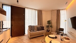 A modern living room with a sofa, dining table, and chairs. There is a TV mounted on the wall and a plant on the table. - VidaCalma Apto 2 (Valencia)