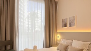 A hotel room with a large bed, a chair, and a view of buildings through sheer curtains. - VidaCalma Apto 2 (Valencia)