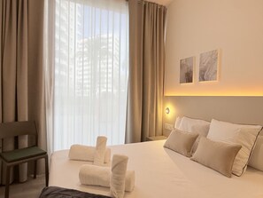 A hotel room with a large bed, a chair, and a view of buildings through sheer curtains. - VidaCalma Apto 2 (Valencia)