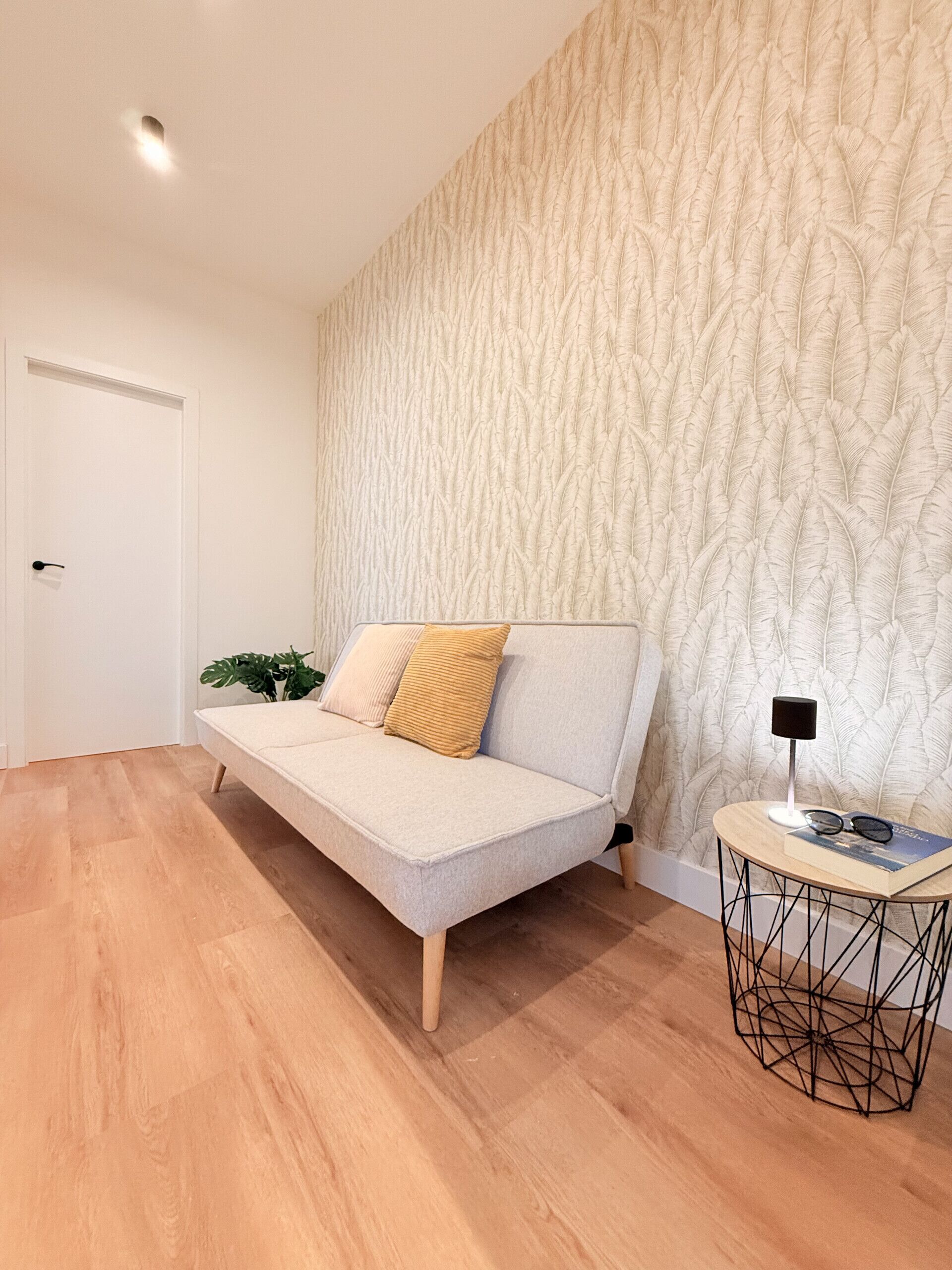 A modern living room with a sofa, a small side table, and a patterned wall.