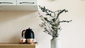 A kitchen with white cabinets, a wooden countertop, a black kettle, and a vase with green plants. - Stylish apartment right by the forest, quiet and close to the center (Chemnitz)