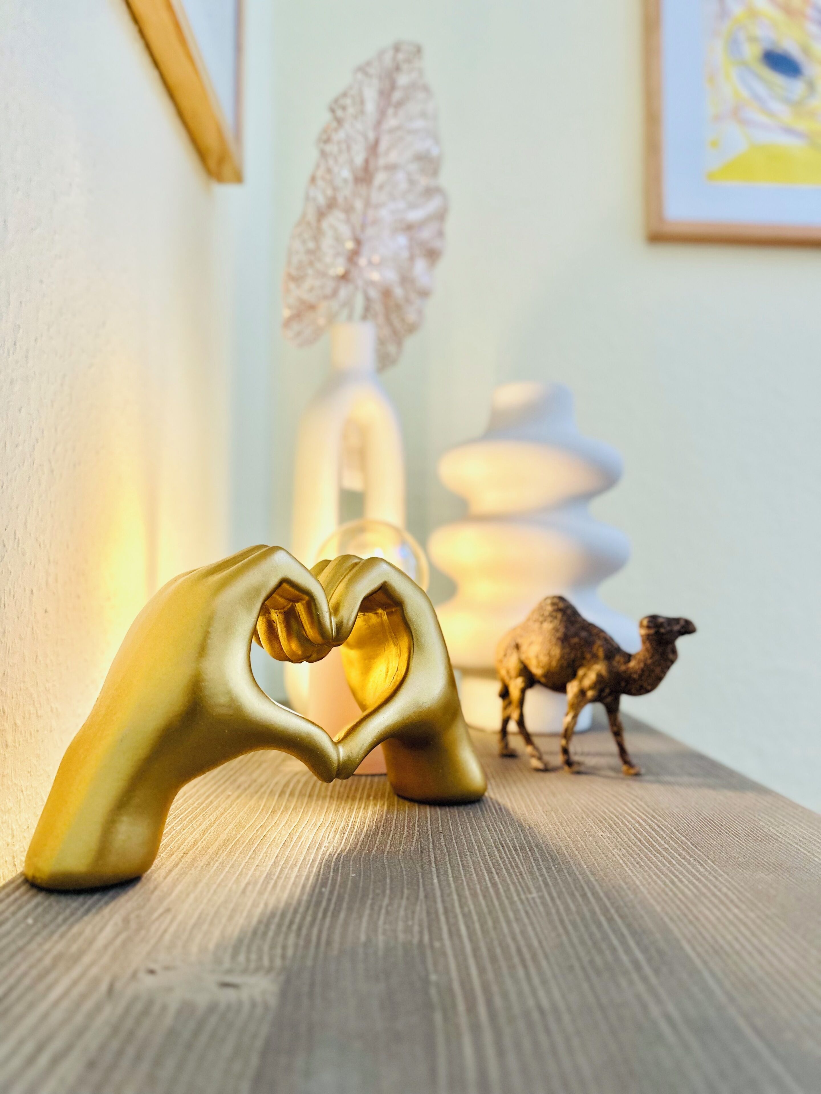 A golden heart-shaped object on a wooden surface with a camel and a white vase in the background.