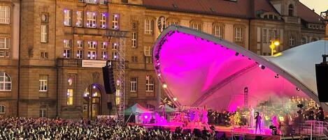 A large crowd gathered in front of a historic building with a stage set up for an event.
