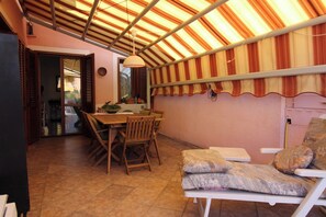 A dining area with a table and chairs, a cushioned bench, and a ceiling with striped fabric. - L' Oleandro - Key to Villas (Valledoria)